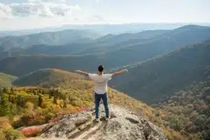 Soft skills – homme ouvrant les mains devant la nature, symbolisant l’épanouissement personnel et la confiance en soi